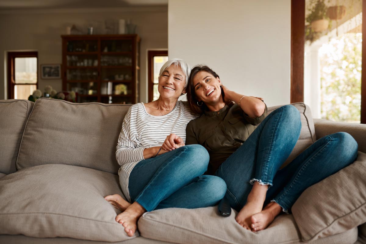 A senior mother wearing Beltone Hearing Aids and daughter sit on the couch together, smiling